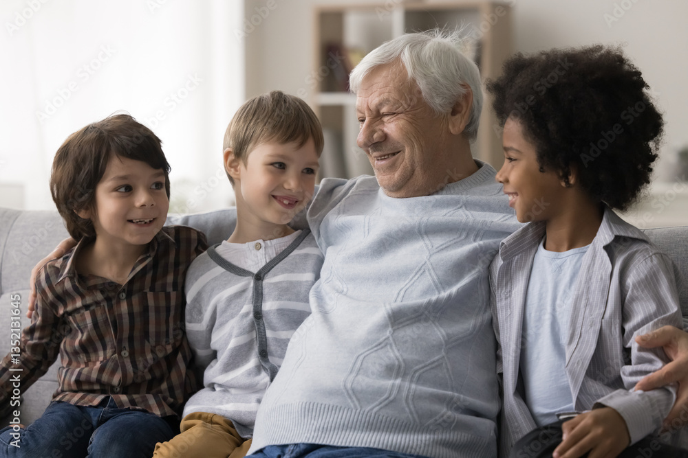 In warm embraces of grandpa. Supportive elderly grandfather hug three beloved little boys multiethnic grandchildren on sofa at living room talk hold conversation listen to kids with interest attention In warm embraces of grandpa. Supportive elderly grandfather hug three beloved little boys multiethnic grandchildren on sofa at living room talk hold conversation listen to kids with interest attention