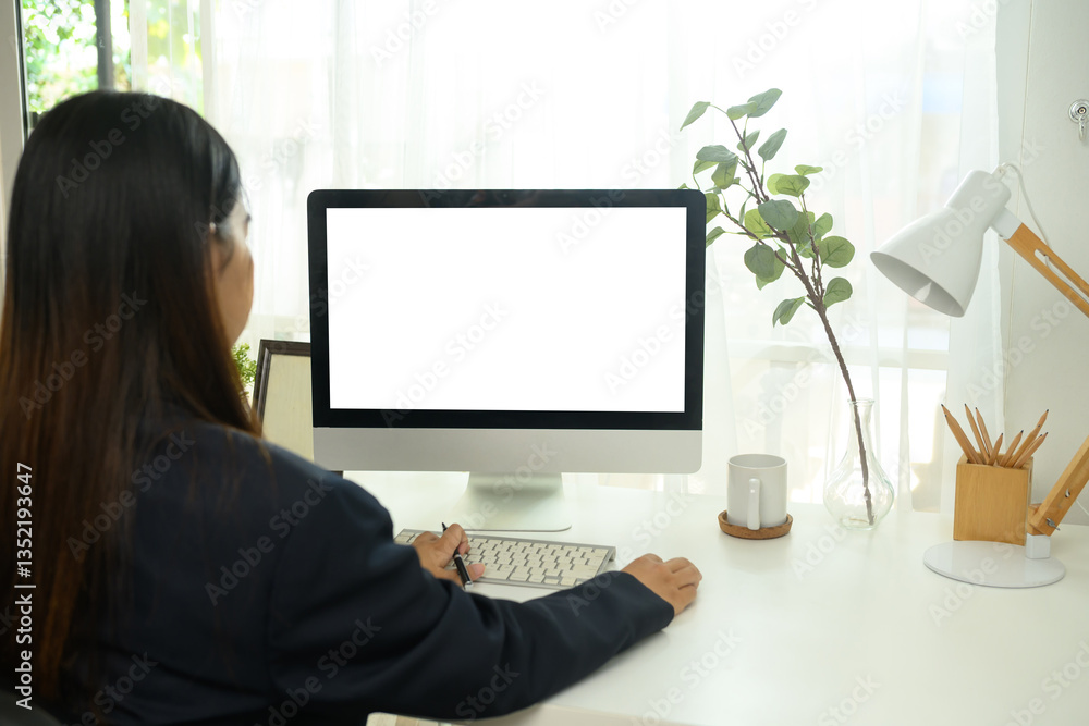 Back view of young businesswoman working on computer in a bright home office Back view of young businesswoman working on computer in a bright home office