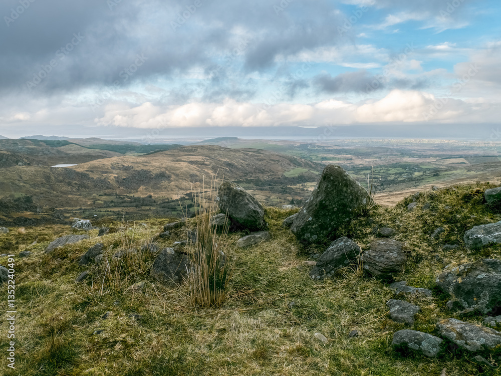 Fototapeta premium Rural setting. Large gray rocks dominate a hilltop. Fields and distant horizon under cloudy skies.