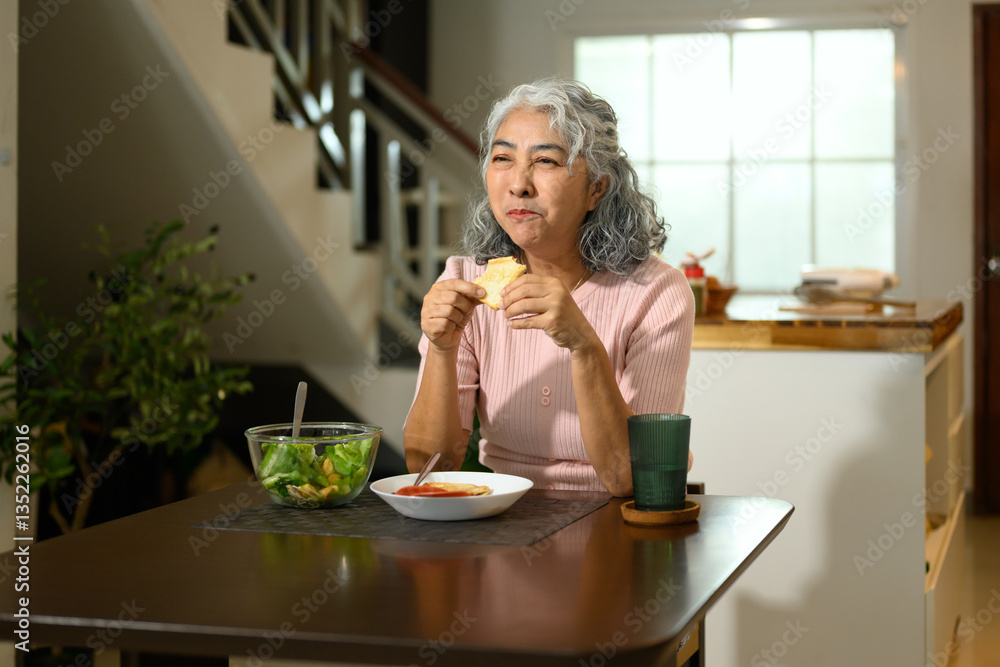Happy senior woman with gray curly hair having a nutritious lunch at a dining table