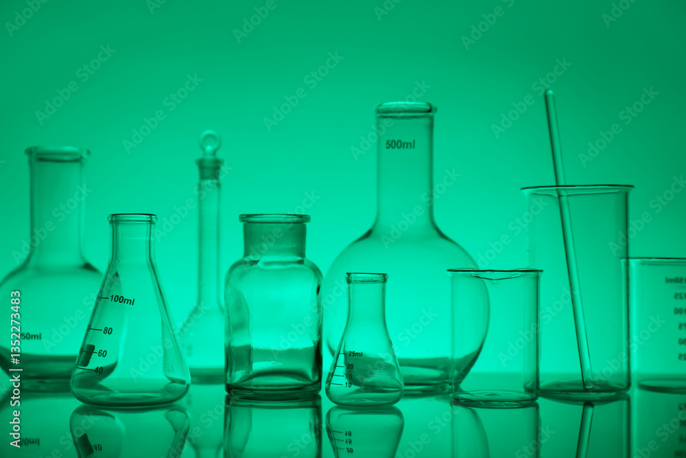 Laboratory glassware on mirror surface against green background Laboratory glassware on mirror surface against green background