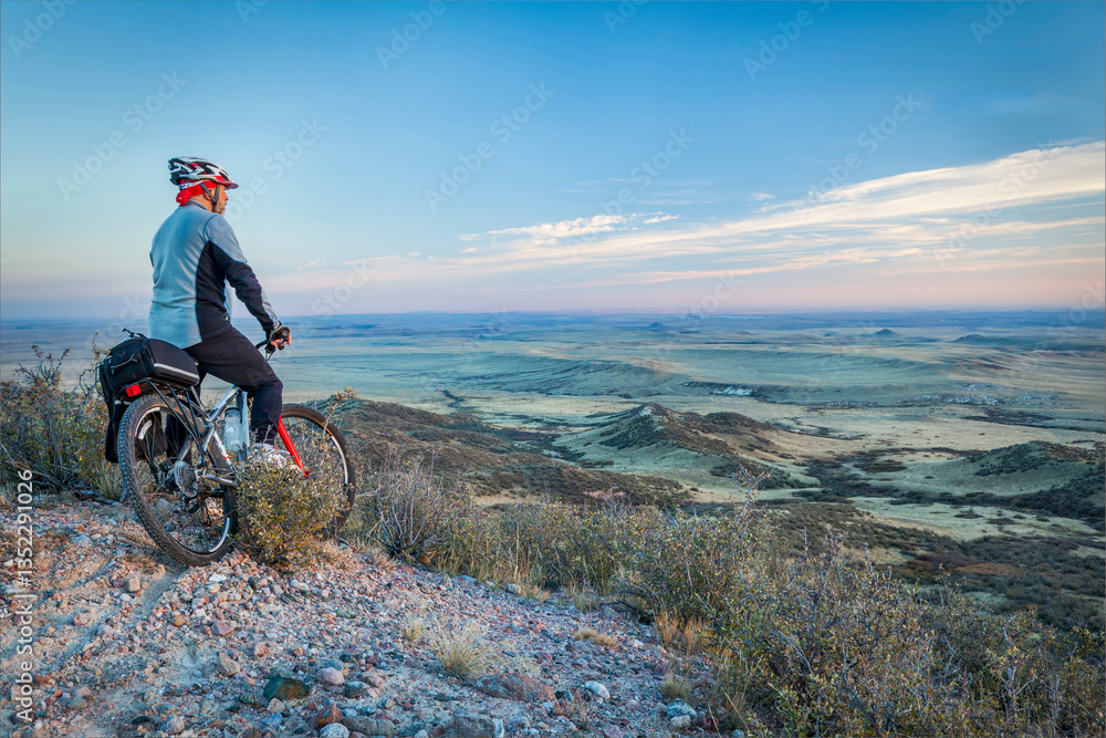 Fototapeta premium senior male on a mountain bike contemplating a view of rolling prairie at dusk, Soapstone Prairie Natural Area near Fort Collins, Colorado