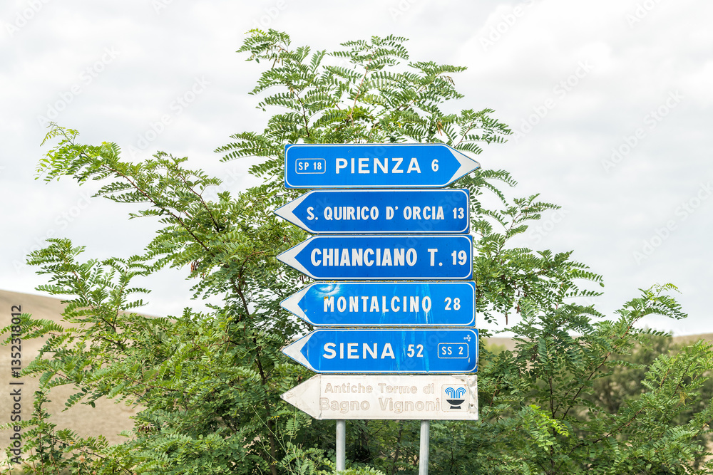 Fototapeta premium Monticchiello, Italy town village in Tuscany during sunny summer day and highway road street with blue exit direction sign for Pienza and Siena