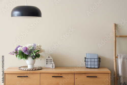 Obraz na plátně Vase with lilacs on wooden chest of drawers and lamp in stylish room, closeup