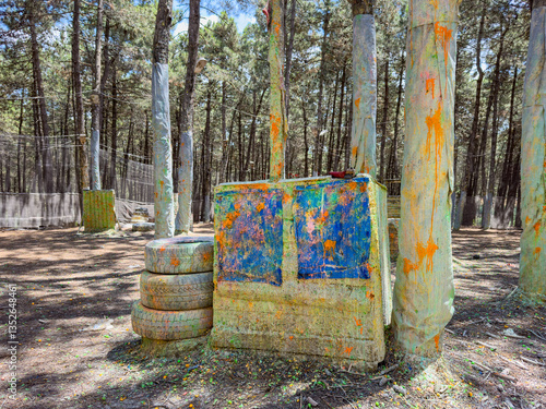 Paintball field with bunkers and trees. Outdoor paintball park challenge arena. Colorful bullet marks. Tactical warfare in nature, battleground. Wooden barrels, cover and shelter in forest