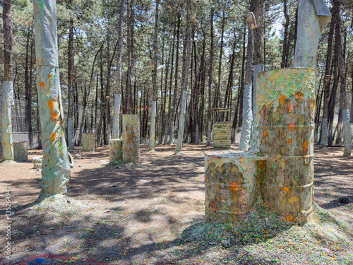 Paintball field with bunkers and trees. Outdoor paintball park challenge arena. Colorful paintball bullet marks. Tactical warfare in nature, battleground. Wooden barrels, cover and shelter in forest