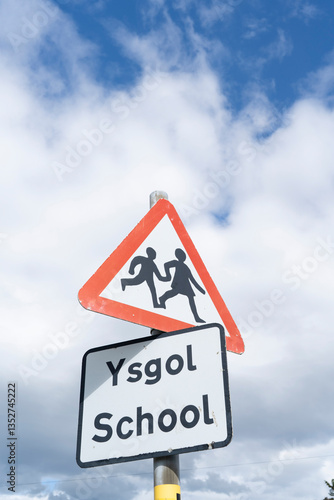 Roadsigns with the symbol for children and the words 'school' in English and Welsh against a cloudy sky.