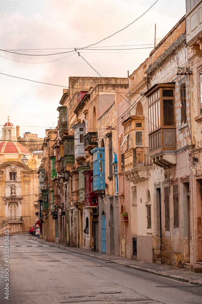 Fototapeta premium The nearly empty St. Margaret Street in Cospicua. Perhaps a reflection of the times. Triq Santa Margerita, Bormla.Cospicua,View at St Paul's Church Cospicua through a street with many colorful bay 