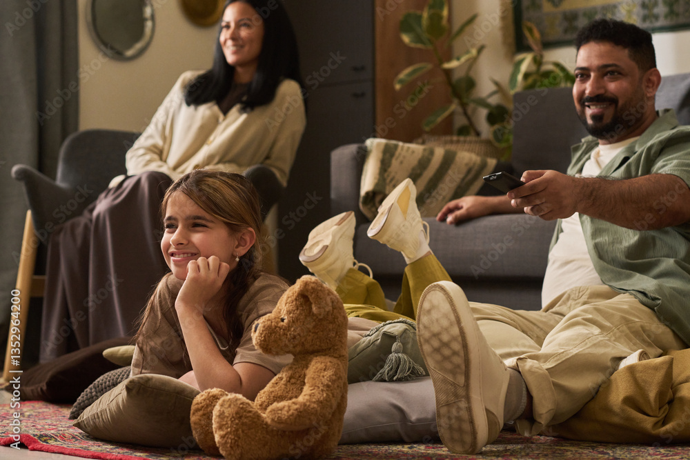 Family enjoying leisure time, sitting comfortably in living room while watching TV and smiling. Plush toy in foreground adds cozy touch to scene