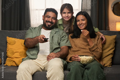 Obraz na płótnie Family enjoying time relaxing on couch while sharing popcorn and smiling. Daughter hugging her parents, showing happiness in comfortable living space w salonie