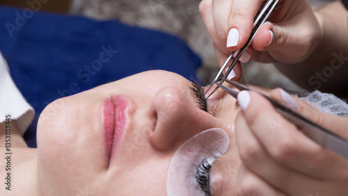 Applying eyelash extensions to a womans eye with tweezers by a beautician