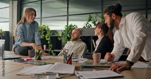 A businesswoman sits on the table engaging in a friendly discussion with her colleagues in a relaxed and professional office setting