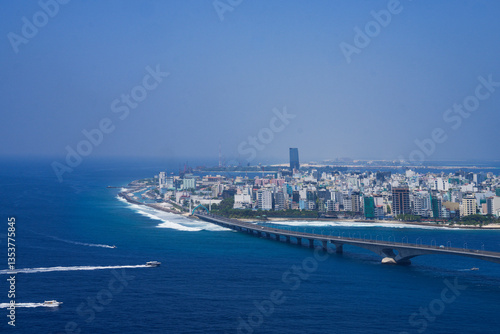 Fototapeta Naklejka Na Ścianę i Meble -  Above City view of Malé City,  the capital of Maldives with Sinamale Bridge located on Male Atoll in the Indian Ocean. from airplane wing flying in the blue sky above Maldives island.
