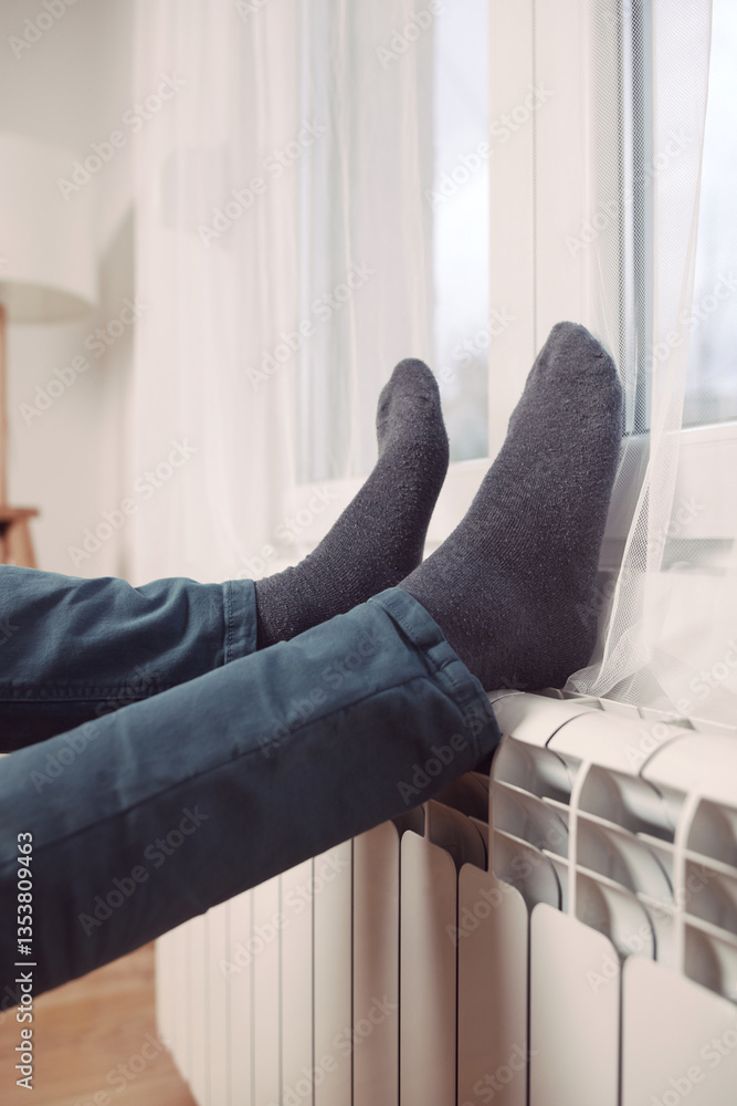 Man's feet with socks on a home heating radiator on a cold winter day outdoors.
