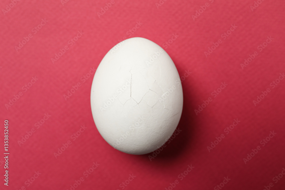 One egg with cracked shell on pink background, top view One egg with cracked shell on pink background, top view