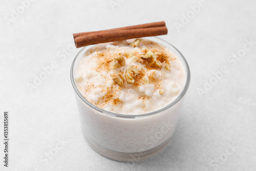 Tasty rice pudding with cinnamon and nuts in glass bowl on light grey table, closeup