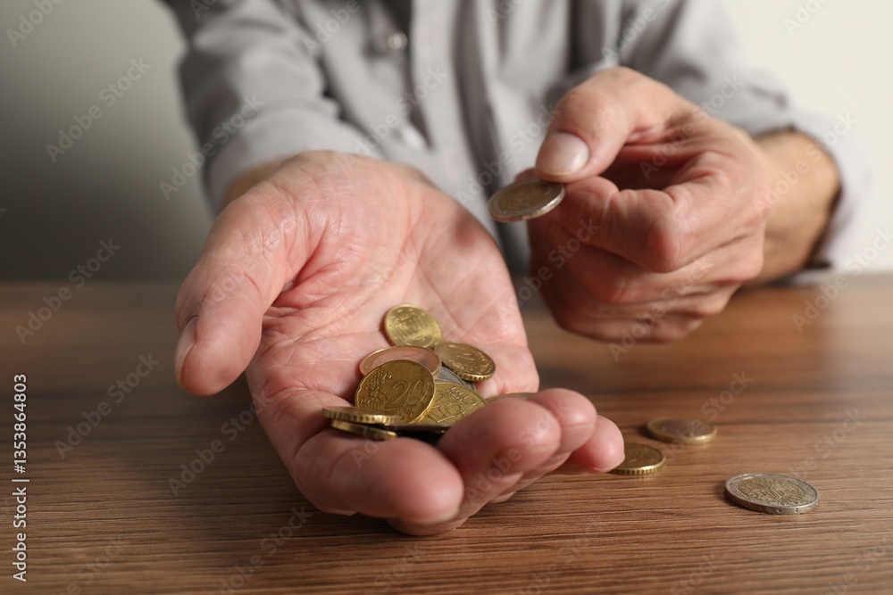 Fototapeta premium Senior man counting coins at wooden table, closeup. Financial problems