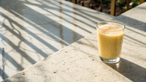 Fresh fruit smoothie in a clear glass cup on a light countertop with beautiful dappled sunlight creating a warm and inviting atmosphere around it