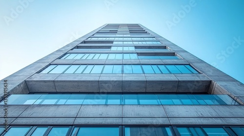 Low-angle view of a modern concrete high-rise building against a clear blue sky.