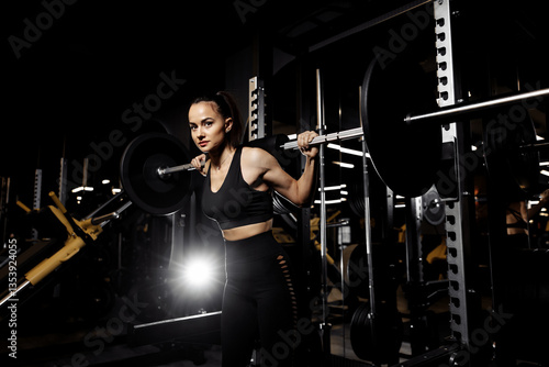 Powerful woman doing squats exercises with heavy barbell in the gym