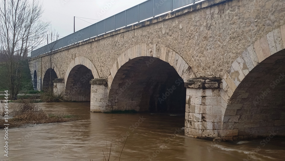 Fototapeta premium Crecida de río por abundantes lluvias atravesando antiguo puente de piedra en Burgos, España