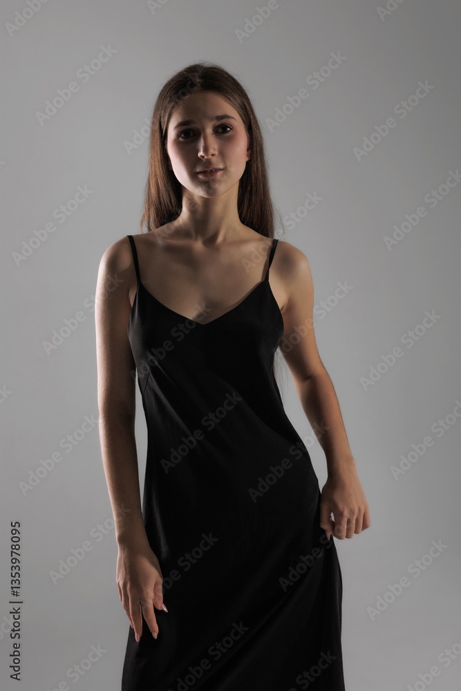 Naklejka premium Model poses confidently in a black dress against a simple gray backdrop during a fashion photoshoot