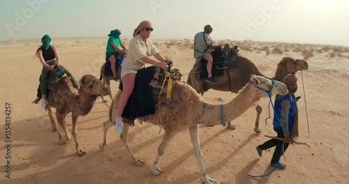 Group Participating in a Camel Ride Adventure in the Sahara Desert with sand storm drifting