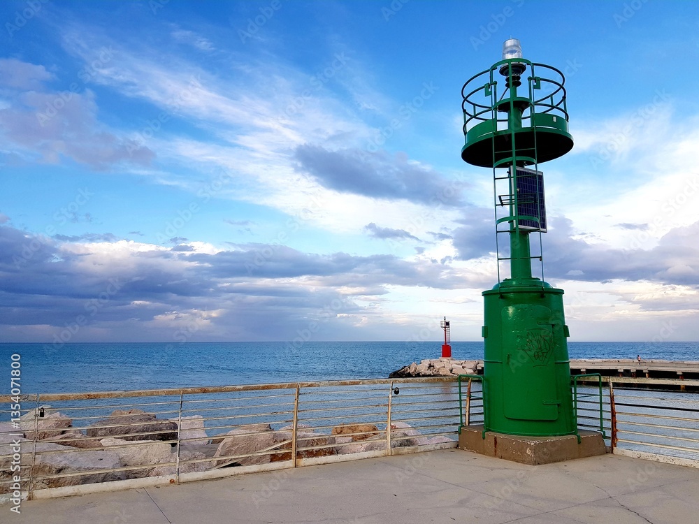 Green lighthouse on the seashore against the blue sky with clouds