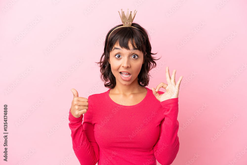 Young mixed race princess with crown isolated on pink background showing ok sign and thumb up gesture Young mixed race princess with crown isolated on pink background showing ok sign and thumb up gesture