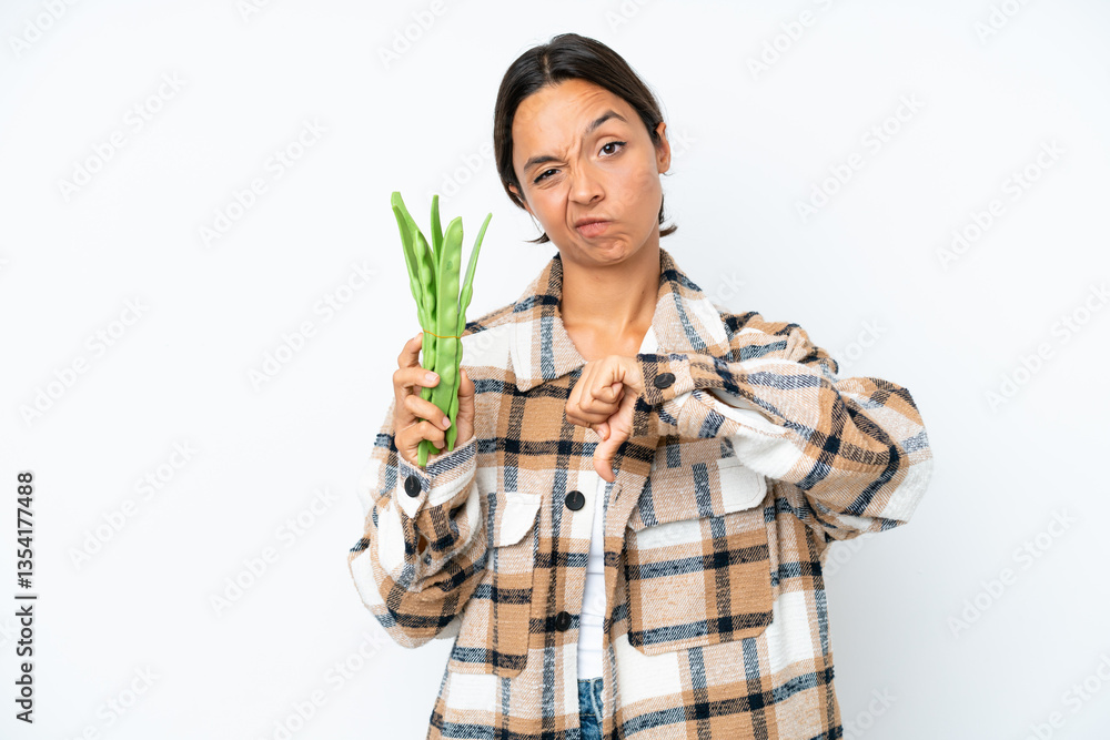 Young hispanic woman holding a green beans isolated on white background showing thumb down with negative expression Young hispanic woman holding a green beans isolated on white background showing thumb down with negative expression