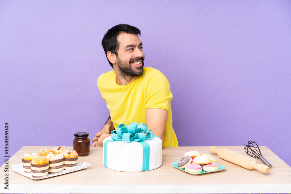Man in a table with a big cake with arms crossed and happy