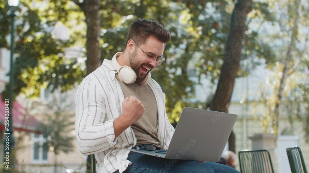 Overjoyed happy young man working on laptop netbook screaming in delight triumph winner gesture celebrate success game money win outdoors. Happy adult guy in glasses sitting on street in city park. Overjoyed happy young man working on laptop netbook screaming in delight triumph winner gesture celebrate success game money win outdoors. Happy adult guy in glasses sitting on street in city park.