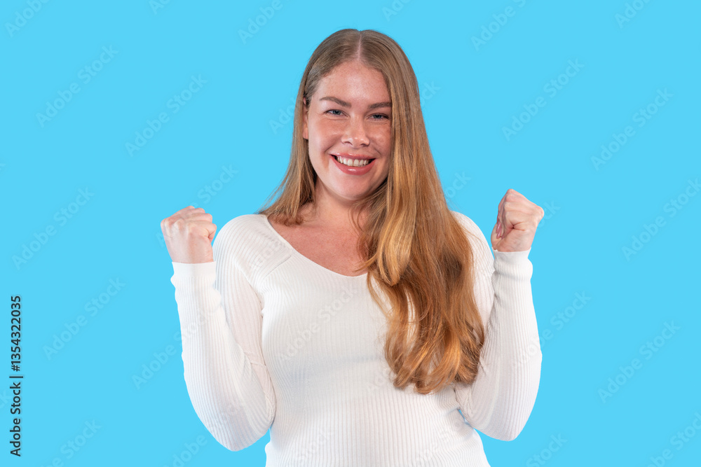 Fototapeta premium Young woman expresses joy and excitement with raised fists against a bright blue background during a celebratory moment