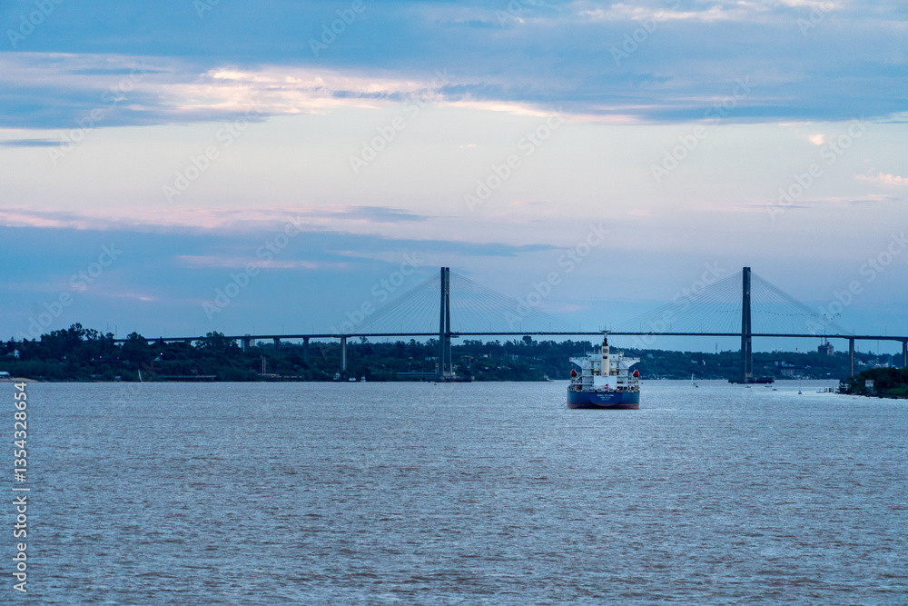 Buque carguero navegando por el río Paraná, con el puente Rosario-Victoria de fondo, al atardecer Buque carguero navegando por el río Paraná, con el puente Rosario-Victoria de fondo, al atardecer
