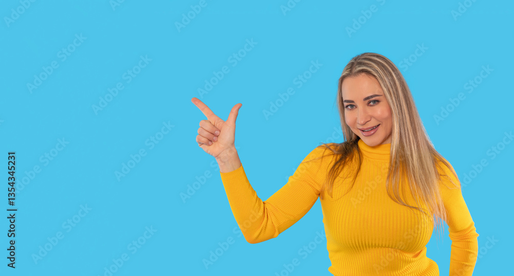 Woman in a bright yellow sweater points confidently with smile against a vivid blue background, showcasing a sense of joy and enthusiasm during a cheerful moment Woman in a bright yellow sweater points confidently with smile against a vivid blue background, showcasing a sense of joy and enthusiasm during a cheerful moment