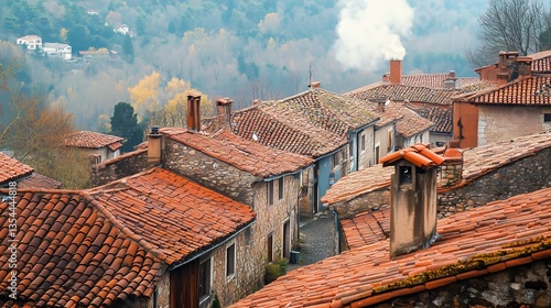 An aerial view of a European village with rows of red clay tiled roofs, chimneys puffing light smoke, and narrow winding streets below
