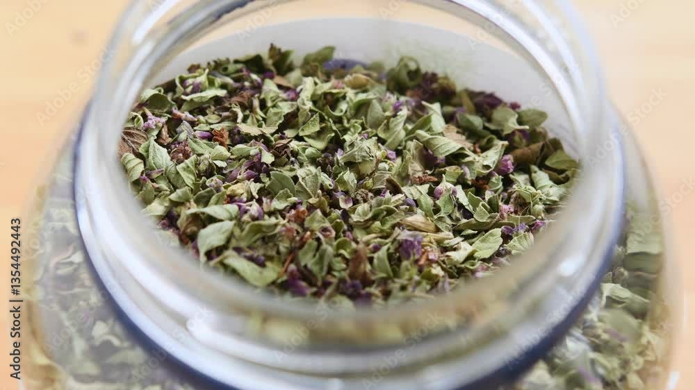 Dried oregano slowly pours into a jar, filling it with natural aroma, suggesting freshness and rustic culinary charm. Dried oregano slowly pours into a jar, filling it with natural aroma, suggesting freshness and rustic culinary charm.