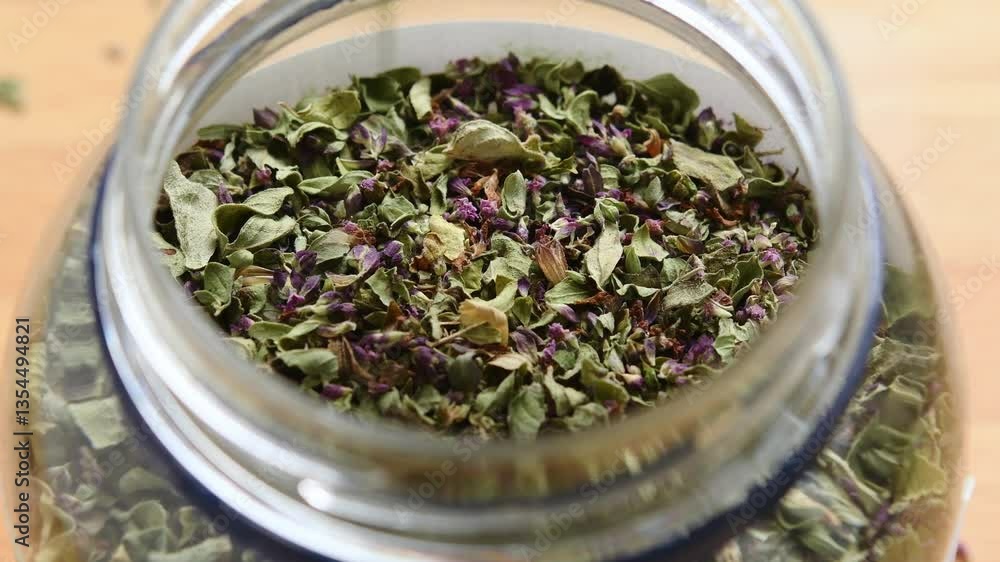 Dried oregano gradually pours into a jar, creating layers of aromatic herbs and highlighting natural kitchen freshness. Dried oregano gradually pours into a jar, creating layers of aromatic herbs and highlighting natural kitchen freshness.