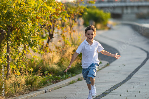 Canvas Print A happy 10 year old boy with outstretched arms runs on the asphalt on the city embankment along the river