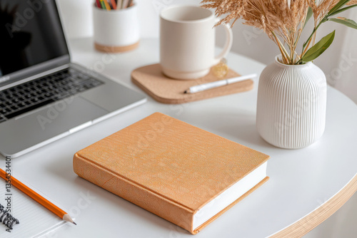 Cozy workspace with closed book, laptop, and coffee on white desk