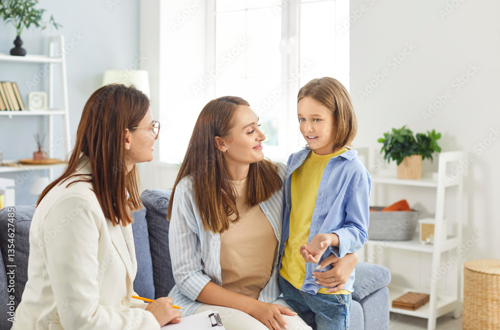 Fototapeta premium Friendly woman psychotherapist or school psychologist talking to preteen child during therapy session at office. Smiling mother hugging her daughter, providing support. Children mental health concept.
