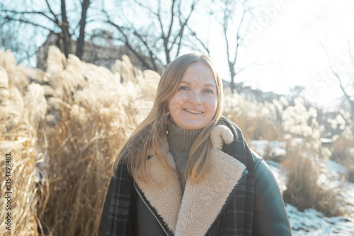 Obraz na płótnie Young blonde cheerful girl in stylish jacket, looking at the camera smiling on a winter day. Close-up delicate white pampas grass swaying in wind. High quality photo w salonie
