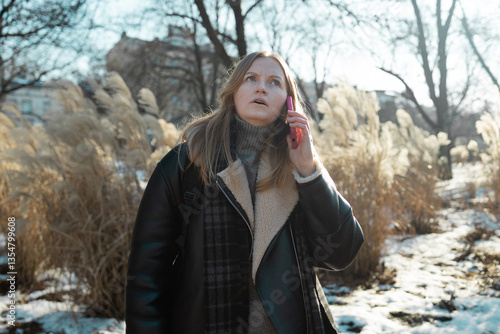 Obraz na płótnie Blonde short hair woman wear blue shirt, hold mobile phone rolling her eyes, omg, wtf standing in the park. Puzzled frustrated girl in shock and look angry, mad. High quality photo w salonie