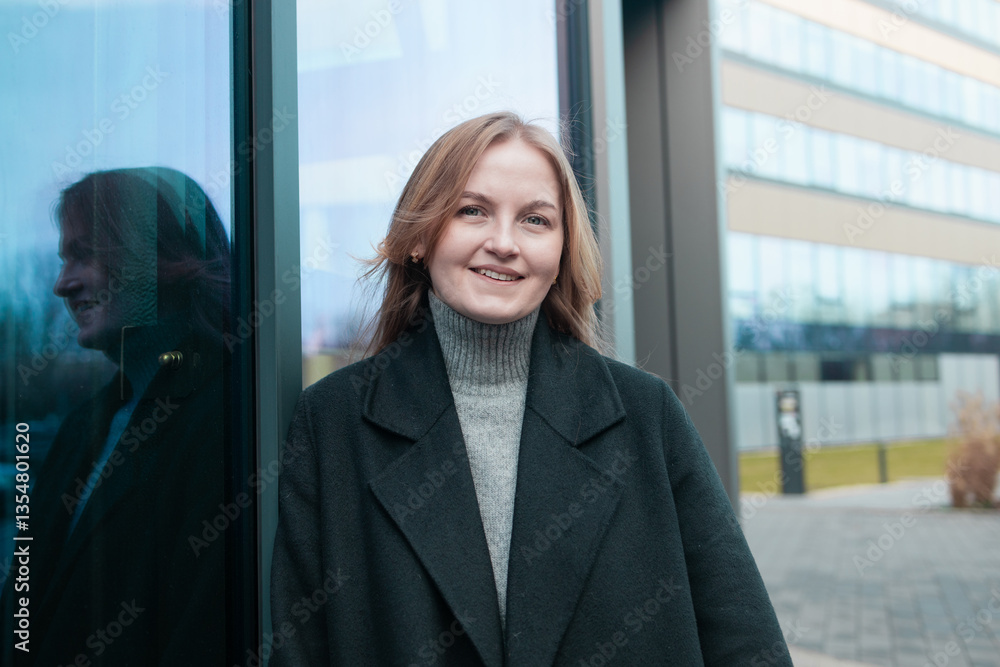 Blonde business lady girl In a stylish black coat standing near business center and looking at camera smiling. High quality photo