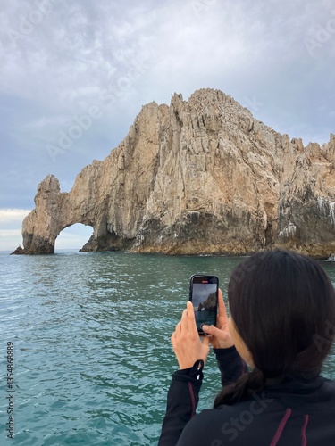 female tourist taking a photo from the sea of the arc at Cabo San Lucas, Mexico.
