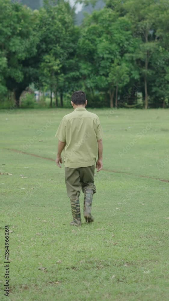 mature Asian man dressed in green and wearing rain boots walking through the grass in a rural area in Vietnam mature Asian man dressed in green and wearing rain boots walking through the grass in a rural area in Vietnam