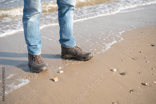 Obraz na płótnie legs of a man in blue jeans, standing on a beach in hiking boots w salonie