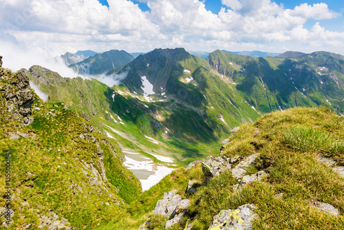 alpine landscape of romania in summer. carpathian adventure. fagaras mountain ridge on a sunny day. scenic valley with snow on the grassy slope beneath a blue sky with clouds. travel to transylvania