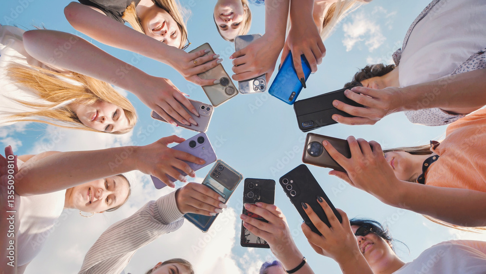 Obraz premium School friends gathering in a circle, using smartphones to share content and have fun together in the outdoors