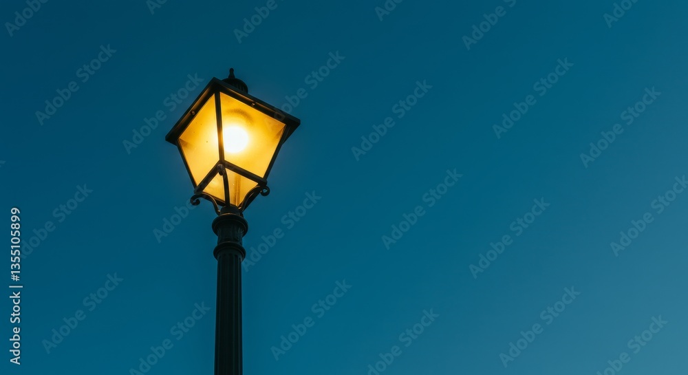 Illuminated Street Lamp at Dusk - A single street lamp glows brightly against a deep blue twilight sky Illuminated Street Lamp at Dusk - A single street lamp glows brightly against a deep blue twilight sky